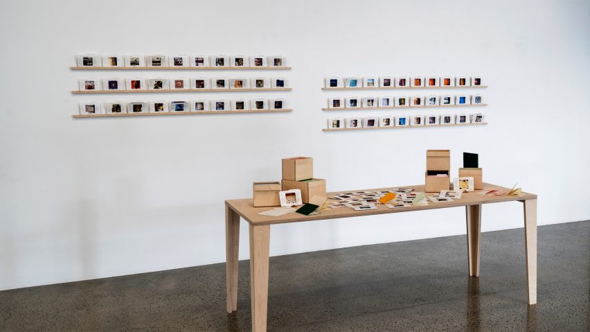 a photograph of a brown wooden table with boxes and pieces of paper on it, with images displayed on a white wall behind it