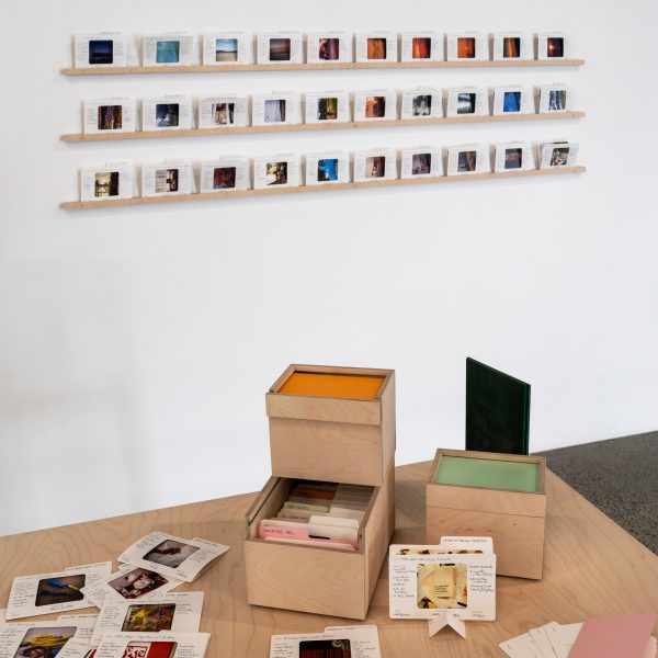 a photograph of a brown wooden table with boxes and pieces of paper on it, with images displayed on a white wall behind it