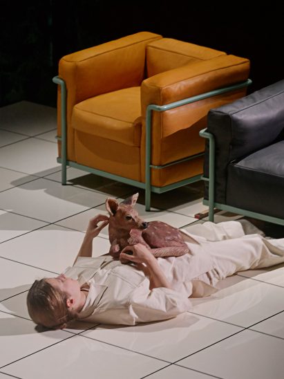 Man with a plastic deer on his chest lying next to a modernist armchair