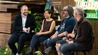 Photo of panel discussion speakers sitting on stools on stage with lumber behind them