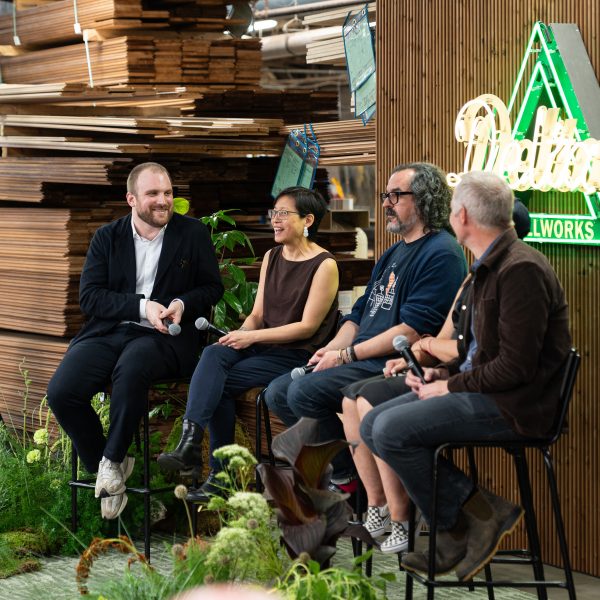 Photo of panel discussion speakers sitting on stools on stage with lumber behind them