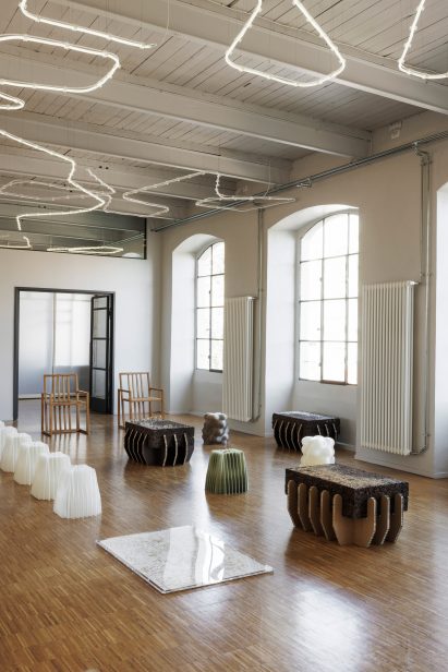 Photo of a large airy space with arched windows, warm wood floorboards and organically shaped furniture-like structures dotted over the floor to make a sitting area