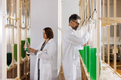 Photo of Claudia Pasquero and Marco Poletto within the algae garden at the Design Apothecary, tending to bioreactor vessels filled with green algae-containing fluid