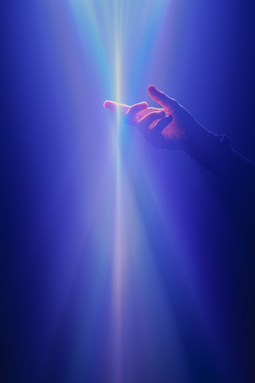 Photo of a hand piercing through a ray of light in Lachlan Turczan's Lucida (I-IV) artwork