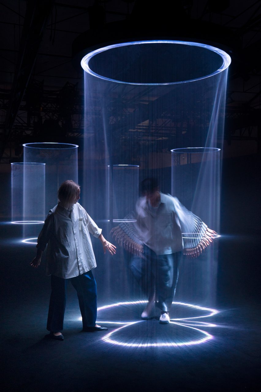 Photo of two people playing under light beam hoops that cast curtains of light into the air in Lachlan Turczan's Lucida (I-IV) artwork