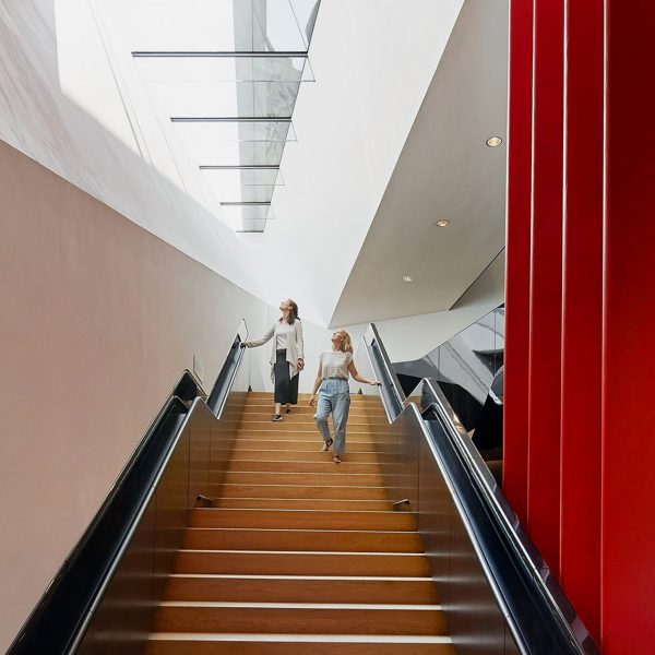 a photograph of two people on a wide wooden staircase in a room with white and red walls.