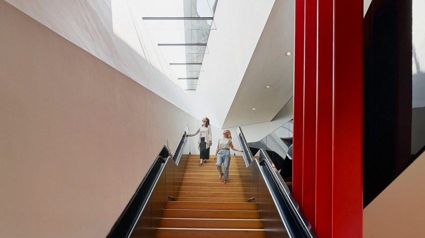 a photograph of two people on a wide wooden staircase in a room with white and red walls.