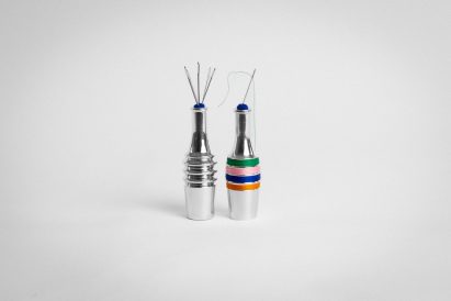 a photograph of two silver bottles. One has coloured thread wrapped around it in tones of orange, blue, pink and green