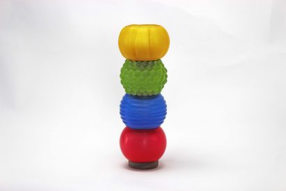 a photograph of a modular lighting system, displaying four lamps on top of each other in a vertical arrangement, in tones of red, blue, green and yellow against a grey backdrop