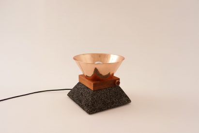a photograph of a lamp in tones of copper and brown against a beige backdrop