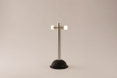a photograph of a lamp built from a plunger, in tones of silver and black against a grey backdrop