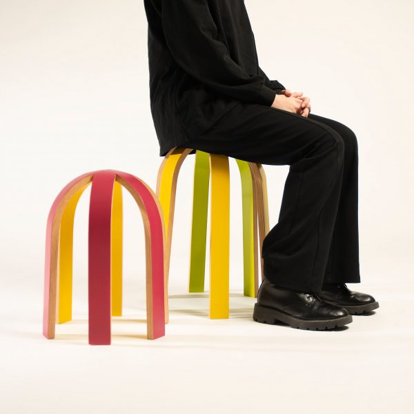 a photograph of a person sat on a stool in an arched shape and in tones of yellow, green and red