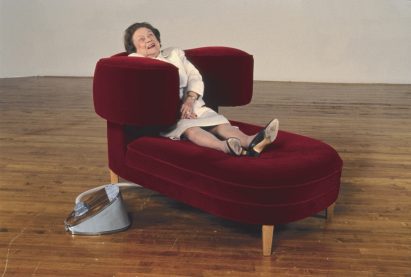 A lady looks delighted while sitting on a red velvet chaise longue