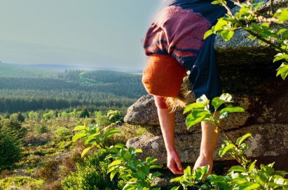 a photograph of a person hanging over a rock in a green landscape