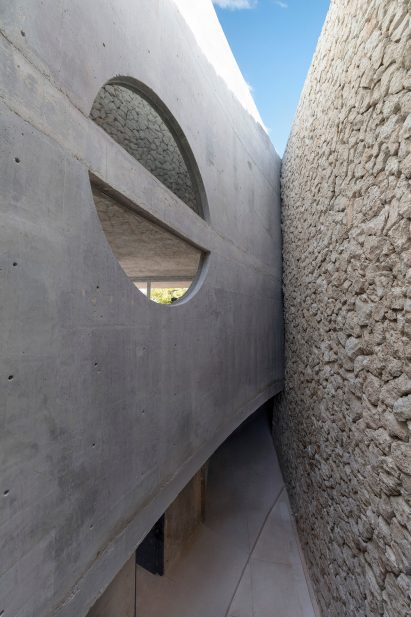 Curved concrete wall with semi-circular windows facing a limestone wall