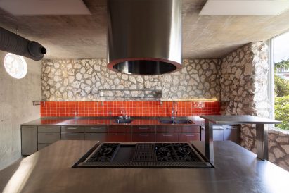 Kitchen with bright red tiles that contrast the natural stone and stainless steel surfaces