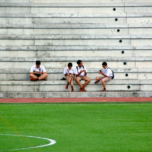a photograph of people sitting on concrete steps beside a green sports pitch