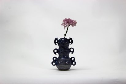 a photograph of a blue abstract-shaped vase with a flower in it