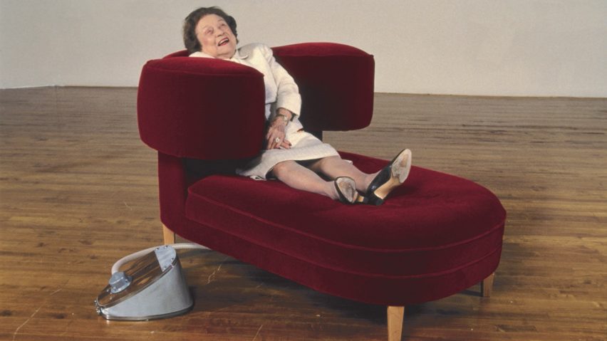 A lady looks delighted while sitting on a red velvet chaise longue