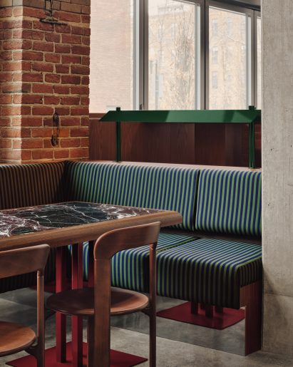 Green and navy striped fabric covers banquettes, and tables feature marble tops and burgundy bases