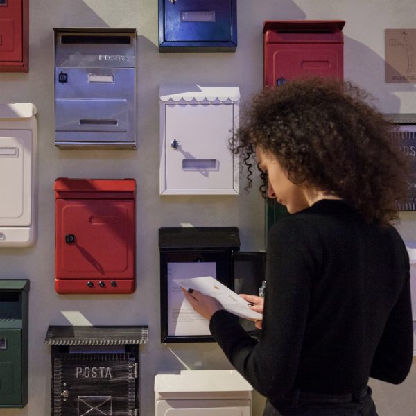 a photograph of a person in front of multiple postboxes in colours of white, red and blue, on a grey wall
