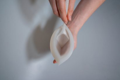 Photo of a person's hands holding a narrow silicon vessel with an angular, deep-bowled spoon resting in it