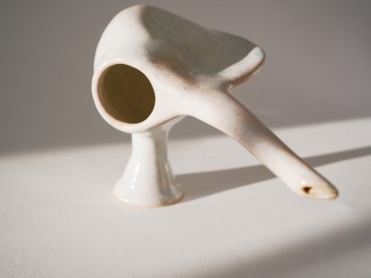 Photo of a strange-shaped ceramic vessel with one foot, a hole on one size, a narrow angular wall opposite that and a long spout