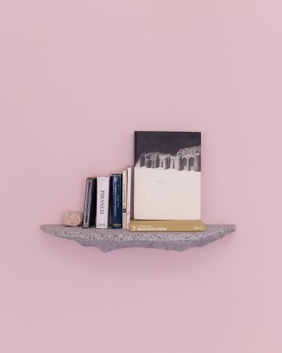 Photograph of the granite-looking, grey shelf holding books against a light pink backdrop.