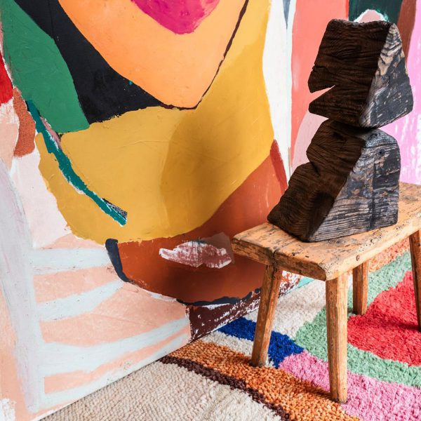 Photo of a wooden table on a colourful rug with a wooden design object on it