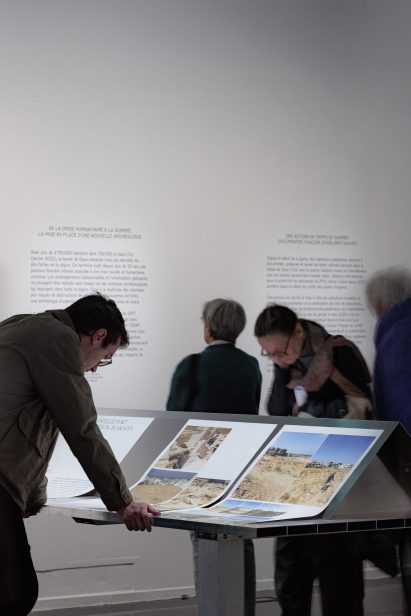 Photo of the Treasures Rescued from Gaza exhibition, showing photographs presented on a display stand made from industrial-looking aluminium sheeting, while visitors view them