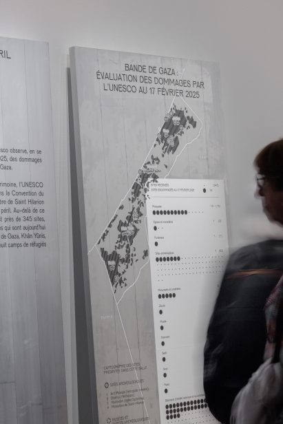 Photo of a person looking at a map of the Gaza Strip printed on a metal background in the Treasures Rescued from Gaza exhibition