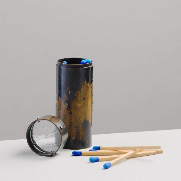 a photograph of a copper matchstick holder with matchsticks laid out next to it