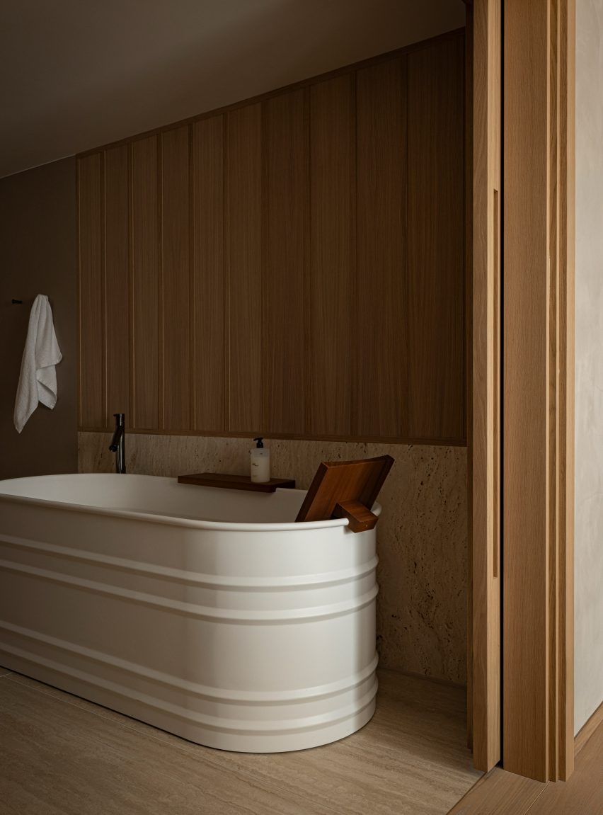 Deep white bathtub and wood-panelled walls