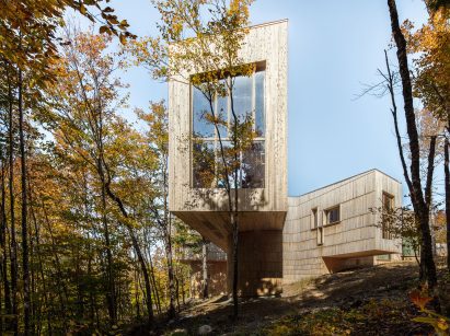 Cedar-clad building in a forest with volumes that cantilever from a central nexus