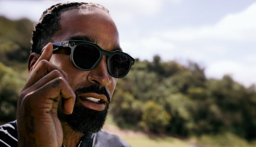 Photo of a man wearing Oakley Meta sunglasses and touching one finger to the arm to activate a function