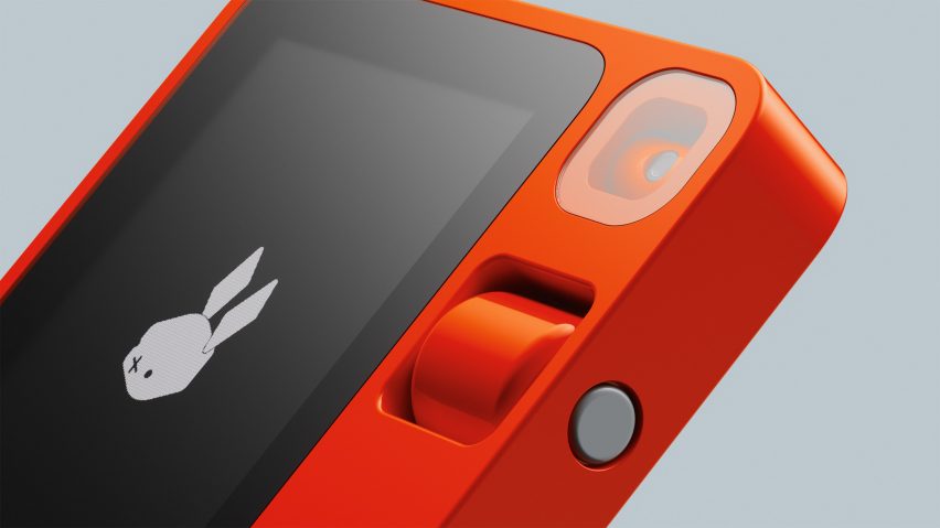 Close-up image of the Rabbit R1 device showing a square bright orange case with a swiveling camera lens and a thumb wheel