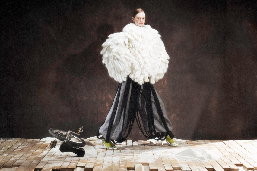 a photograph of a model wearing a white feathered garment and black trousers