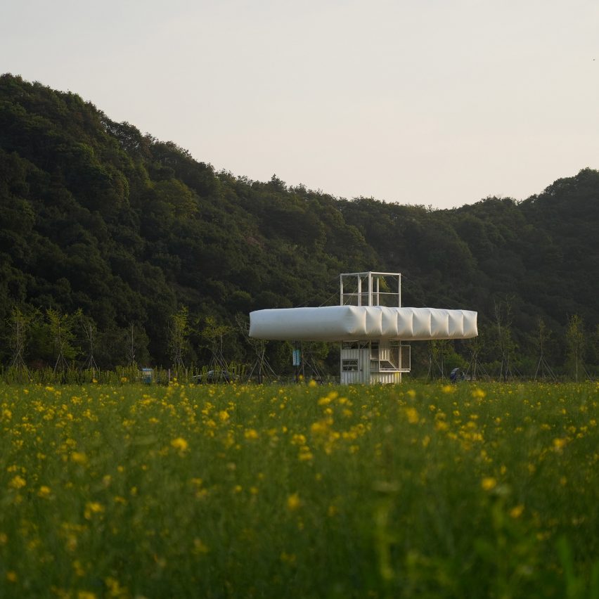 A large white cantilevered inflatable pavilion in an open green field set against a treeline