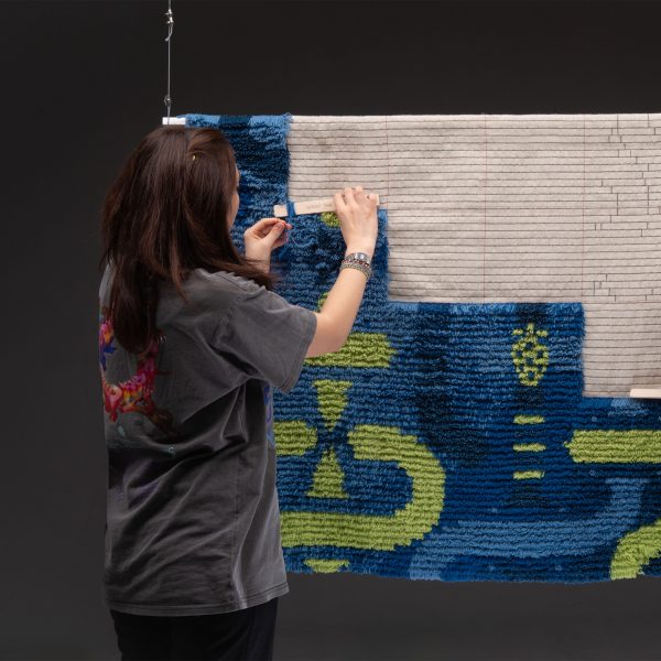 a photograph of a person tending to a tapestry in tones of blue, green and beige
