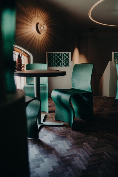 Restaurant interior with dark wooden parquet floors and green 3D printed chairs