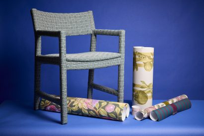 a photograph of a chair and rolls of fabrics against a blue backdrop