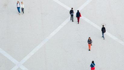 Aerial photo of people walking alone or in pairs or standing still in a vast concrete public space