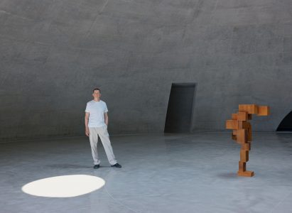 Antony Gormley standing beside artwork at concrete gallery within Museum SAN