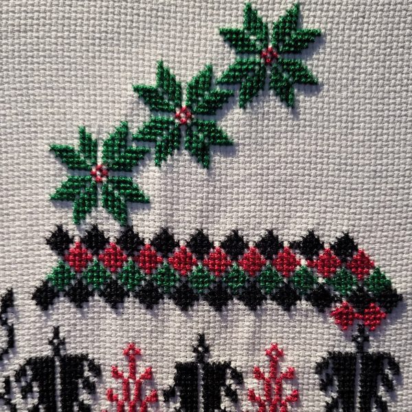 a photograph of a cross stitch in tones of black, green and red