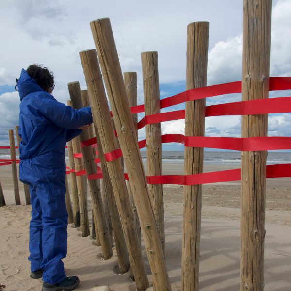 Photo of red ribbon between wooden sticks on a beach, with a person in a blue suit