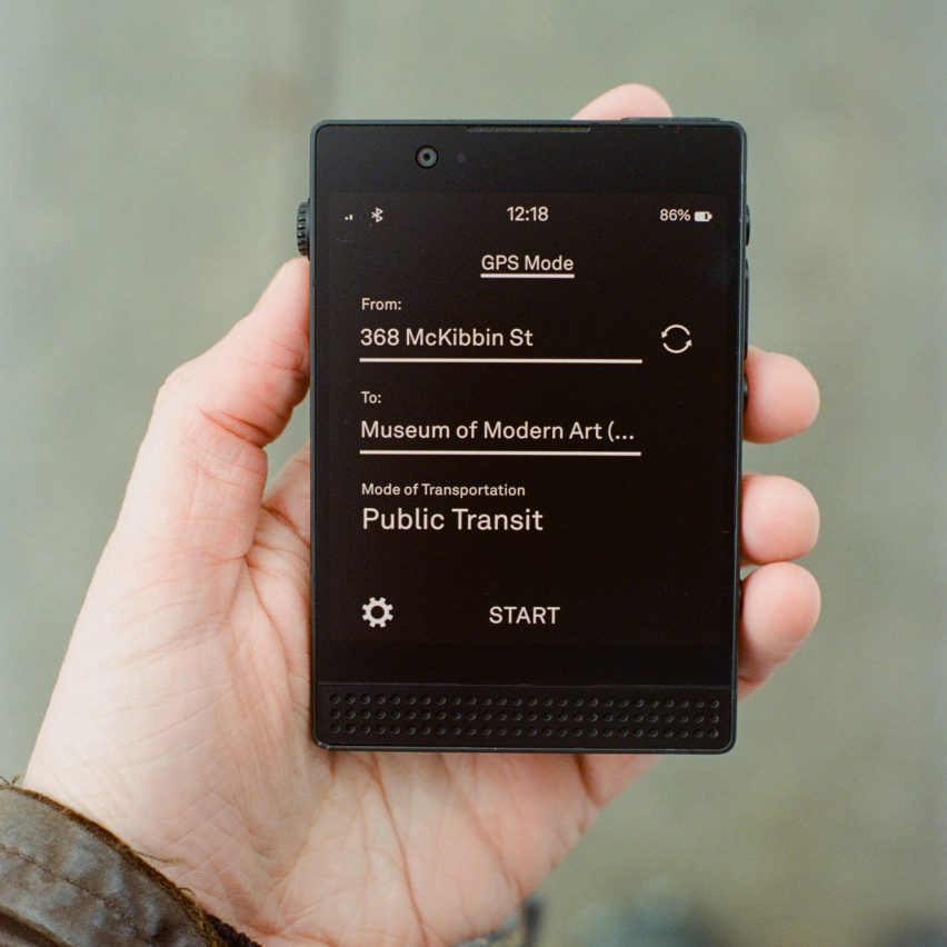 Photo of a person's hand holding a Light Phone 3 showing the directions app, with white text on a white background reading 'From 368 McKibben Street' 'To Museum of Modern Art' and a mode of transportation field set to 'public transit'. Below that a text button reads 'start'