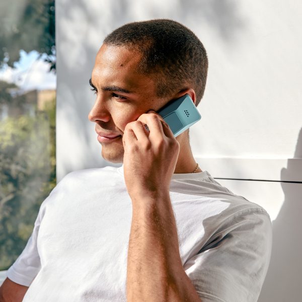 Photo of a man holding a light blue Punkt MP02 phone up to his hear while on a call
