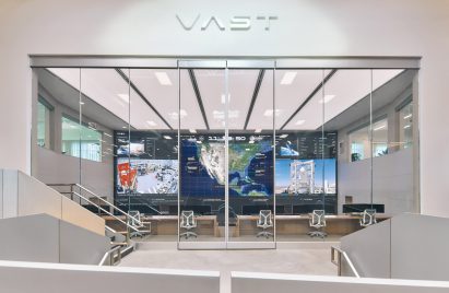 Photo of the Vast headquarters, looking in at a wall-to-wall, floor-to-ceiling colour screen in the mission control centre from a viewing platform outside in the communal area