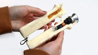 Photo of the opened casing of the WoolTech torch proof of concept, showing a darker coloured section where the biomaterial has been carbonised, and a battery and light bulb pressed into the other side