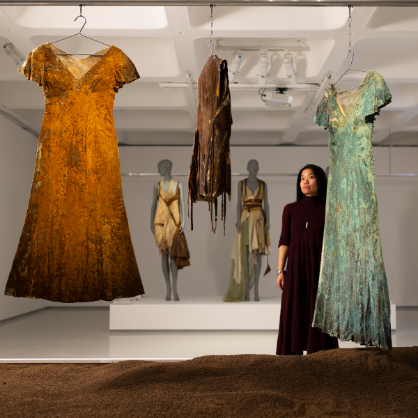 Woman looking at dirt-covered dresses hanging in gallery space